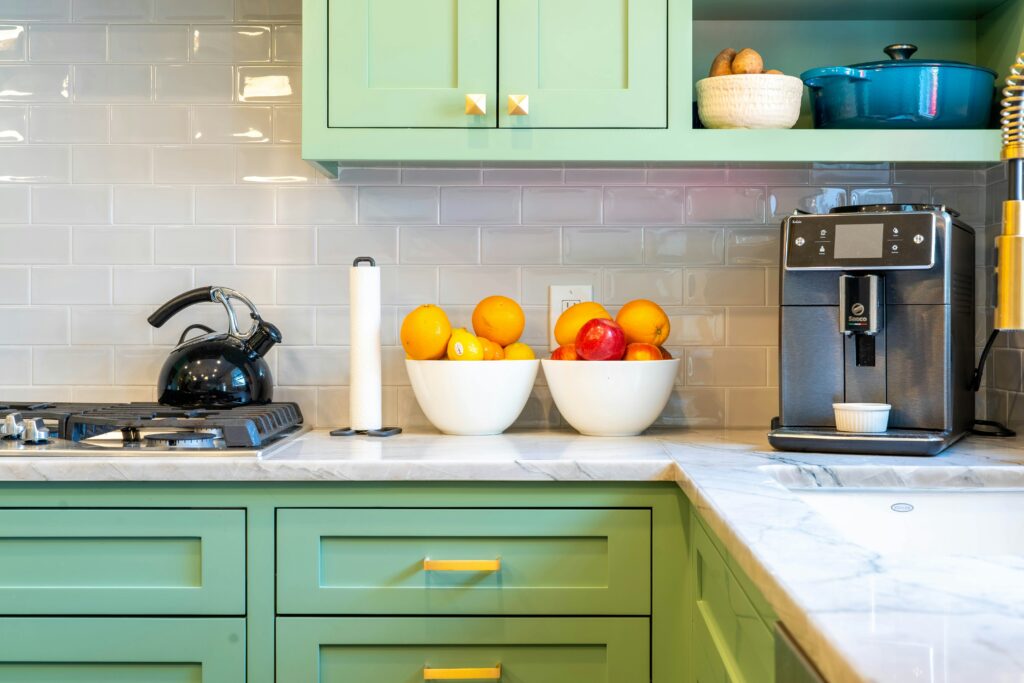 A pristine, modern kitchen for an all inclusive house share in Cheltenham, featuring green cabinets, a coffee machine, and fresh fruit.